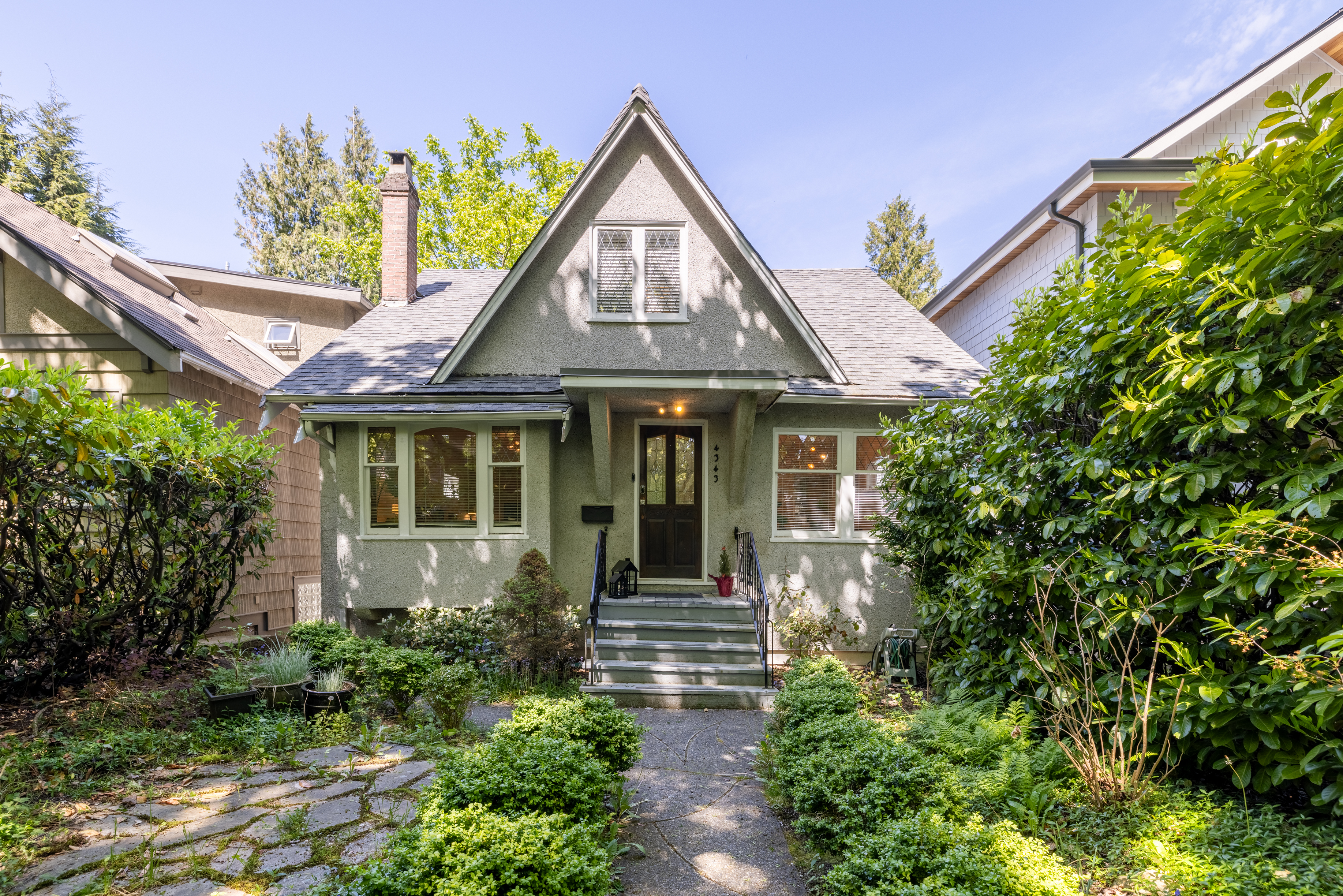 The front facade of 4343 West 11th Avenue — a stucco character home with steep gabled roof, leaded glass windows and lush garden.